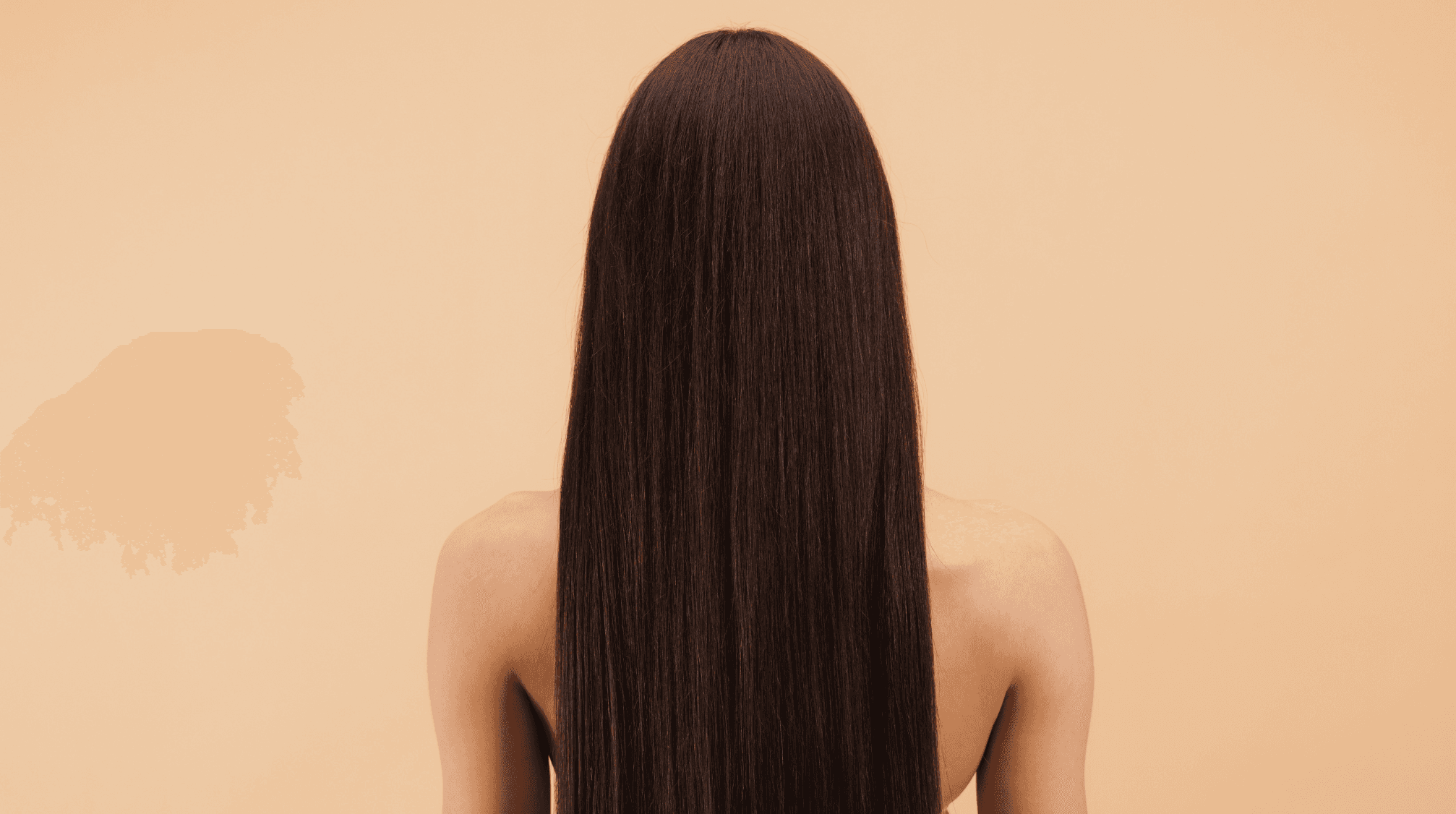 Vue de dos d'une femme aux longs cheveux bruns, droits et brillants, posant sur fond beige, représentant la beauté et le soin des cheveux